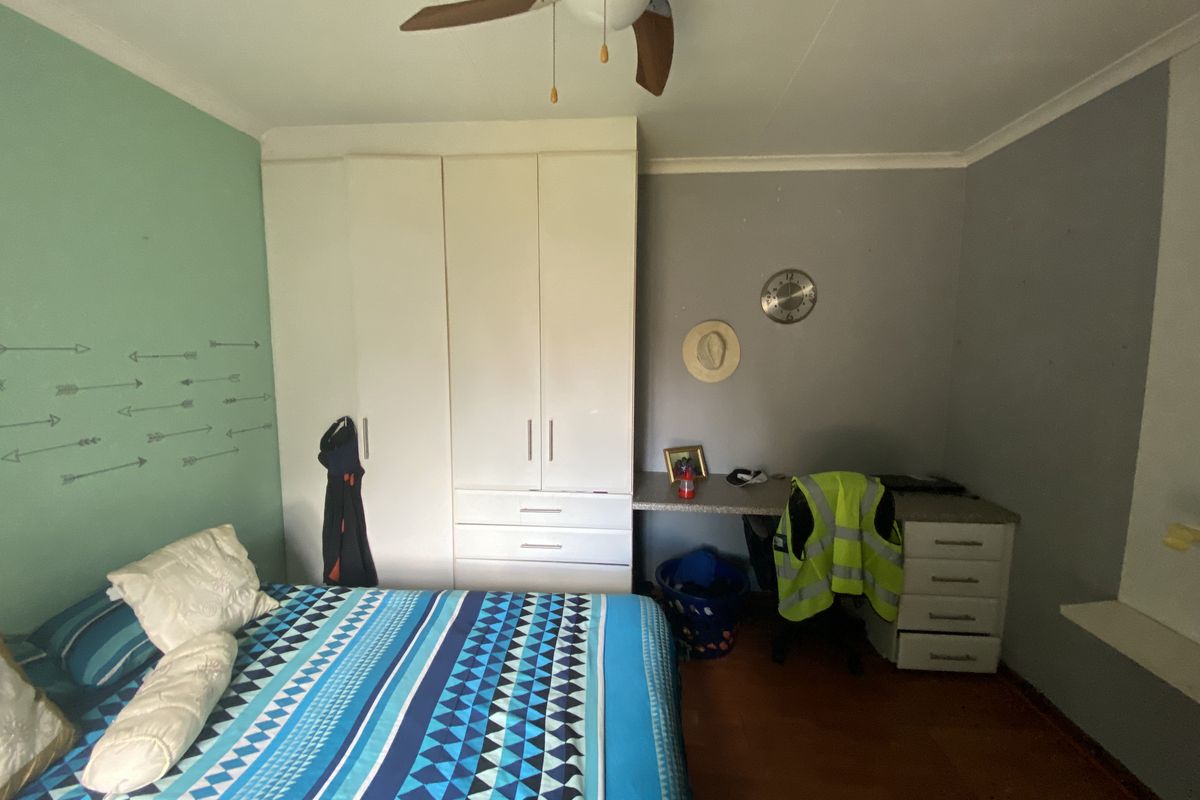 A bedroom featuring a built-in wardrobe, integrated desk space, and a ceiling fan, with painted accent walls and traditional flooring.