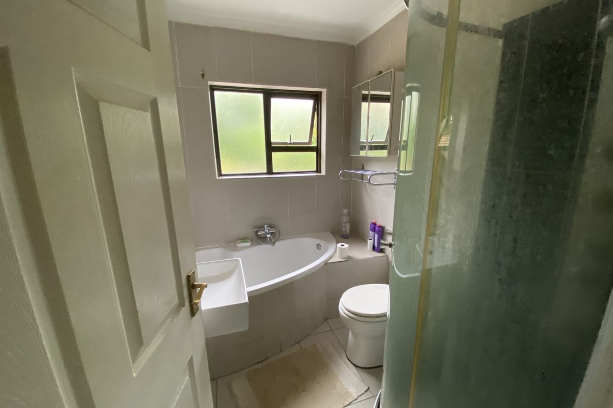 A functional bathroom featuring a corner bathtub, separate shower enclosure, wall-mounted basin, and toilet with neutral wall and floor tiling.