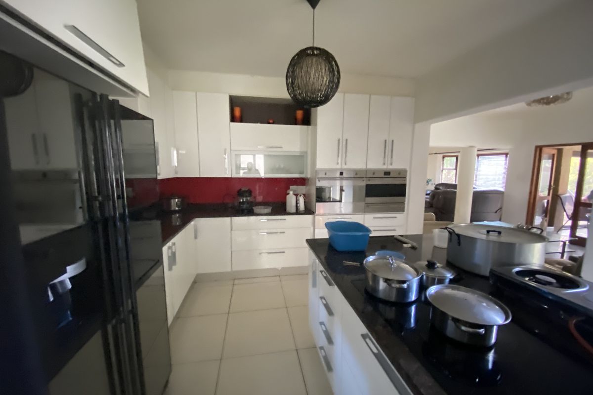Modern kitchen featuring white cabinetry, dark stone countertops, a central island, and integrated appliances, flowing into an adjacent living area.
