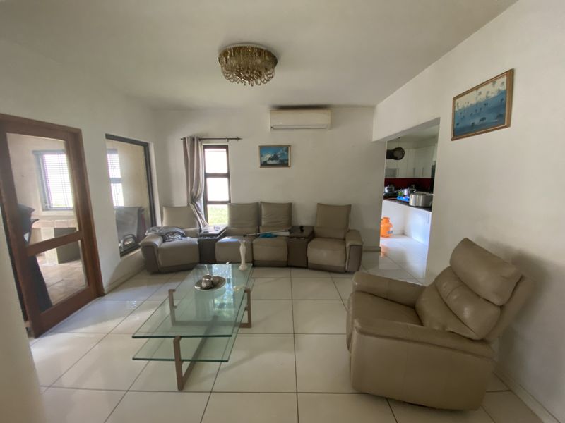 Open-plan living area featuring tiled flooring, a split-system air conditioner, and a crystal chandelier, with an adjacent view into the kitchen area.