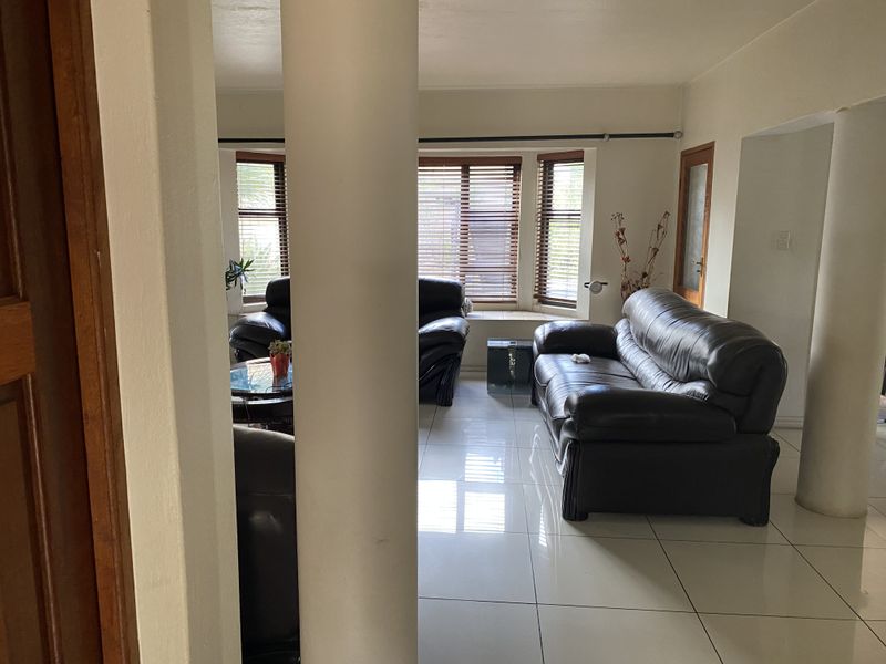 Spacious living room featuring large format floor tiles, structural columns, and a bay window with venetian blinds.