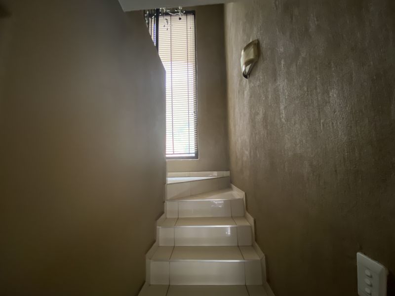 A staircase featuring tiled steps and a wall-mounted light fixture, illuminated by natural light from a window with venetian blinds.