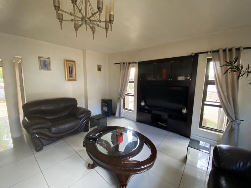 A living room featuring tiled flooring, a built-in dark wood entertainment unit, and a central chandelier, offering a functional and well-lit space.