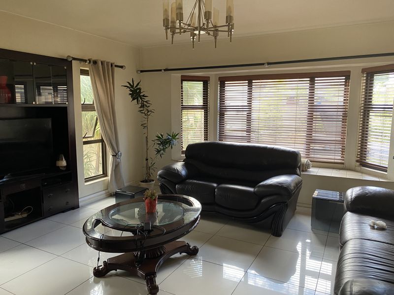 A spacious living room featuring large windows with venetian blinds, tiled flooring, and built-in cabinetry, offering a bright and functional living space.