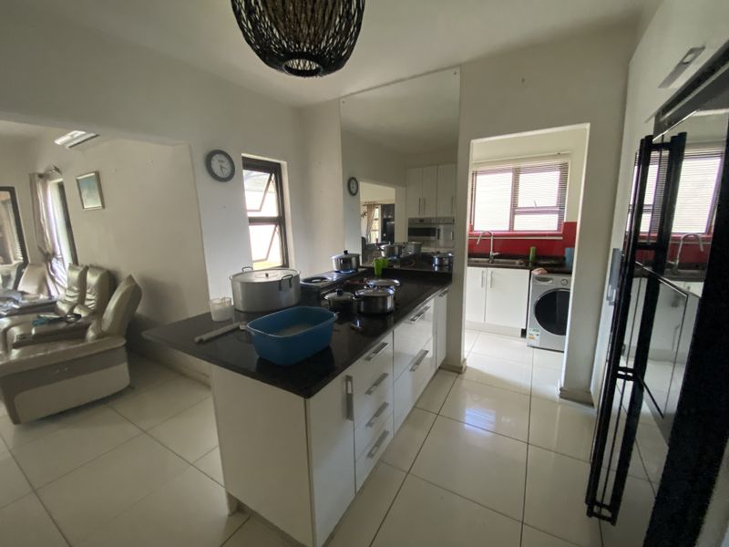 Open plan kitchen featuring a central island with granite countertops, adjacent to a functional scullery area with tiled flooring throughout.