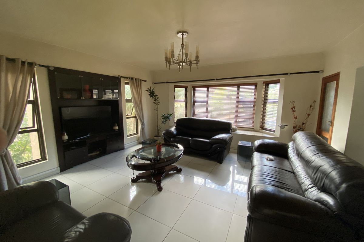 Spacious living room featuring large bay windows, polished tile flooring, a built-in media cabinet, and a central chandelier.