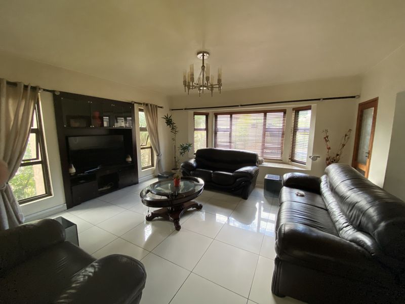 Spacious living room featuring large bay windows, polished tile flooring, a built-in media cabinet, and a central chandelier.