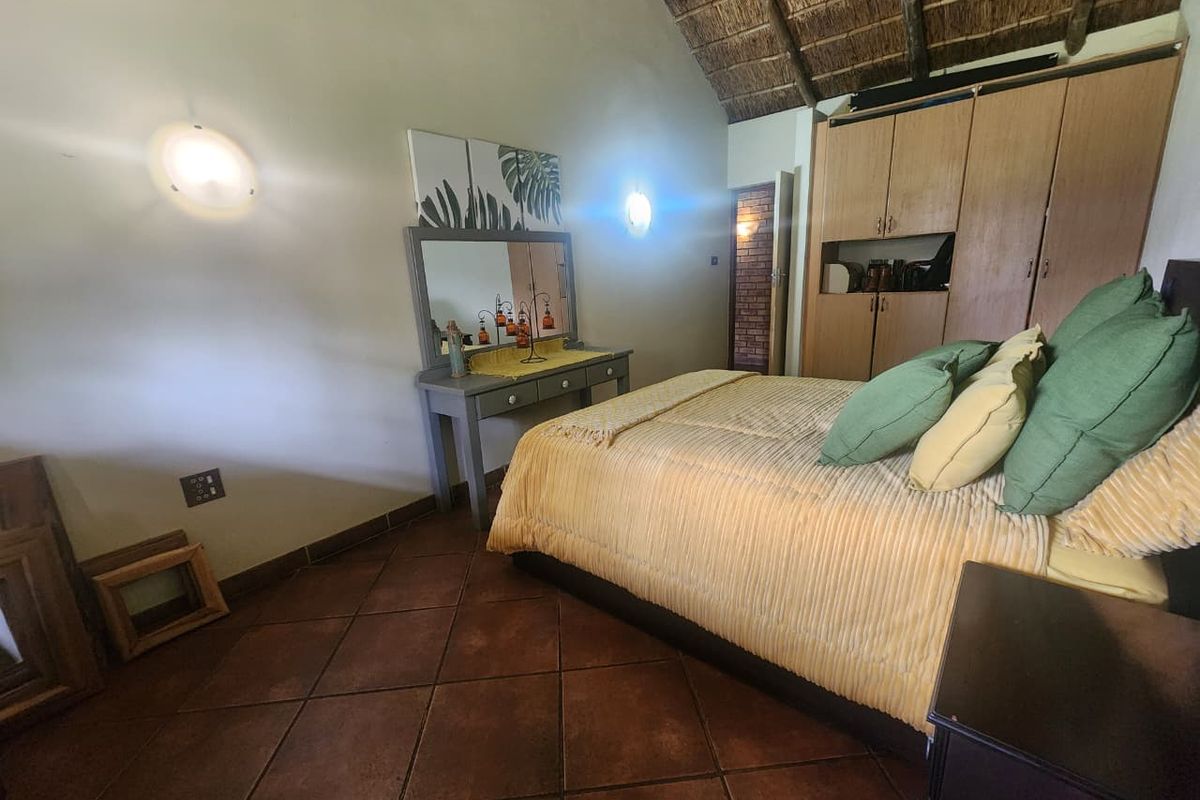 A bedroom featuring a high vaulted thatched ceiling, built-in wooden cabinetry, and terracotta floor tiles.