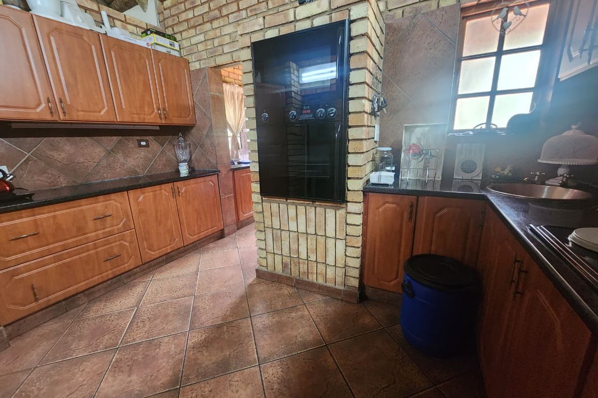 A rustic kitchen featuring wooden cabinetry, dark granite countertops, a built-in oven, and tiled flooring with a distinctive brick feature wall.