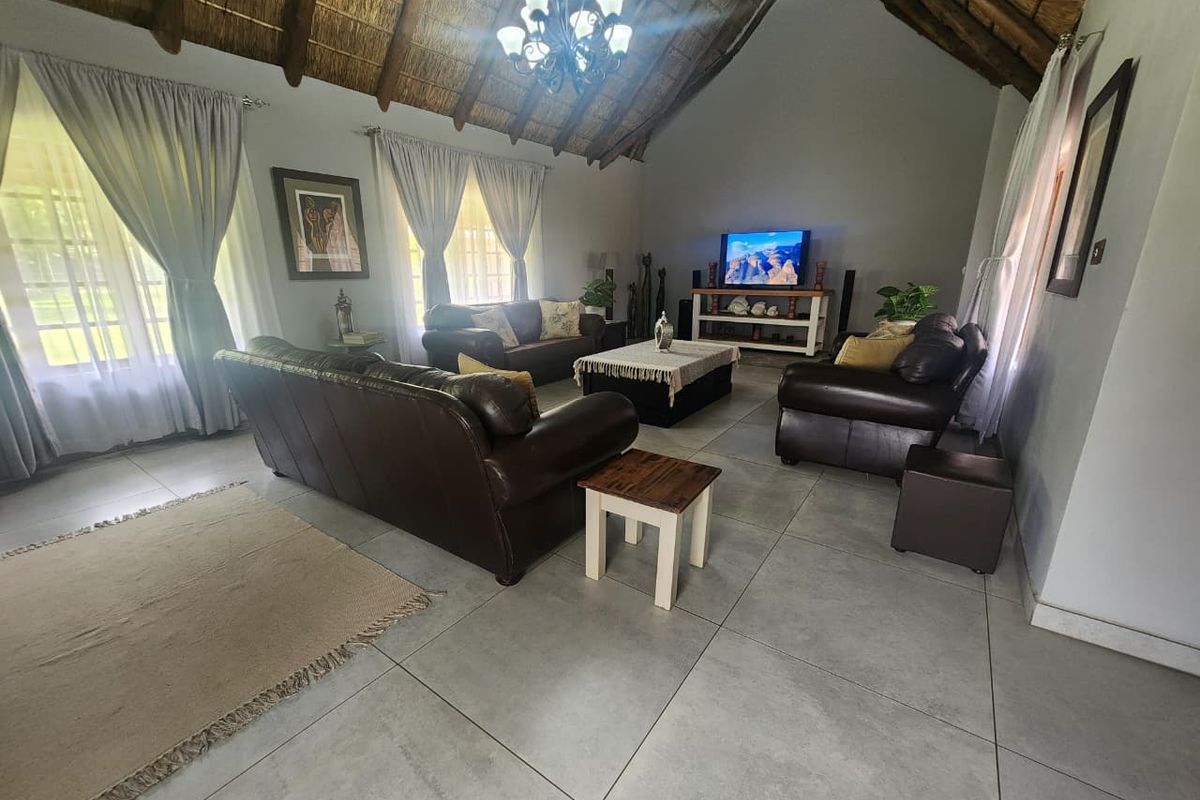 Spacious living room featuring a high vaulted thatched ceiling, large windows, and neutral floor tiling, creating an airy and inviting atmosphere.