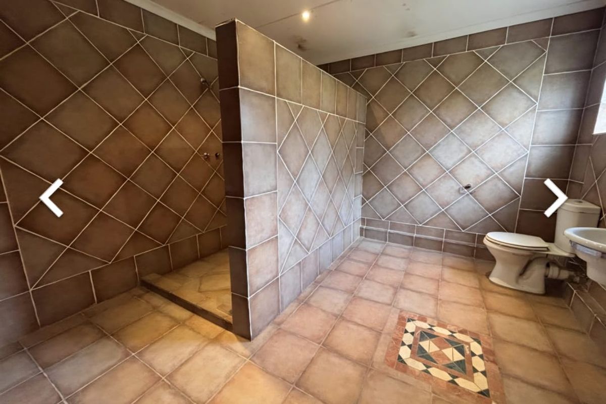 A spacious bathroom featuring a walk-in shower enclosure, a standard toilet, and a wall-mounted basin, finished with decorative tiled walls and flooring.