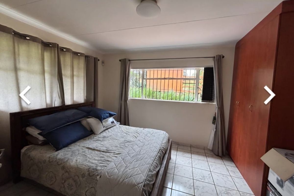 A bedroom featuring built-in wooden cupboards, tiled flooring, and security bars on the windows.