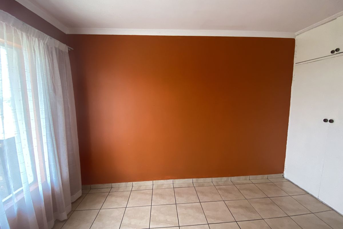 An empty bedroom featuring tiled flooring, built-in cupboards, and a large window with curtaining.