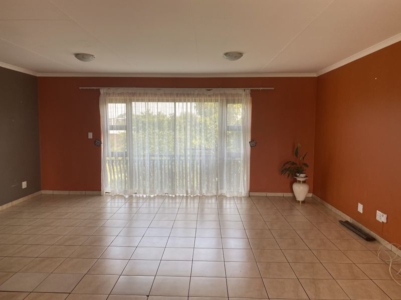 A spacious, empty living room featuring neutral tiled flooring and a large sliding glass door that provides natural light and access to the outdoors.
