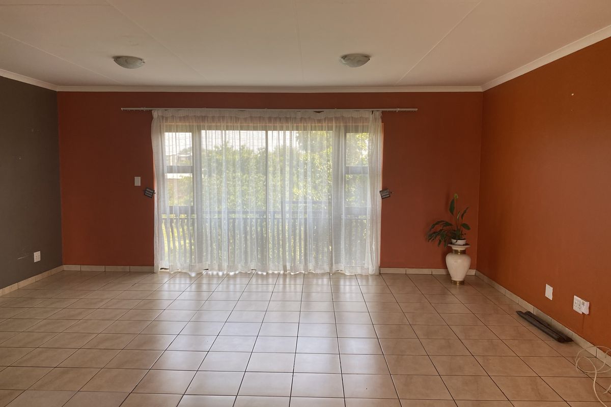 A spacious, empty living room featuring neutral tiled flooring and a large sliding glass door that provides natural light and access to the outdoors.