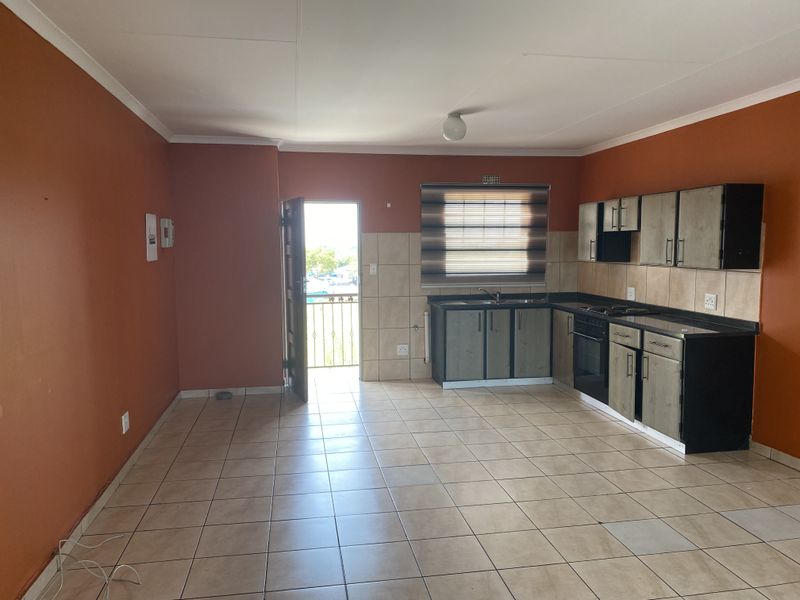 Open-plan kitchen and living area featuring tiled flooring, built-in cabinetry with integrated oven, and direct access to a balcony.