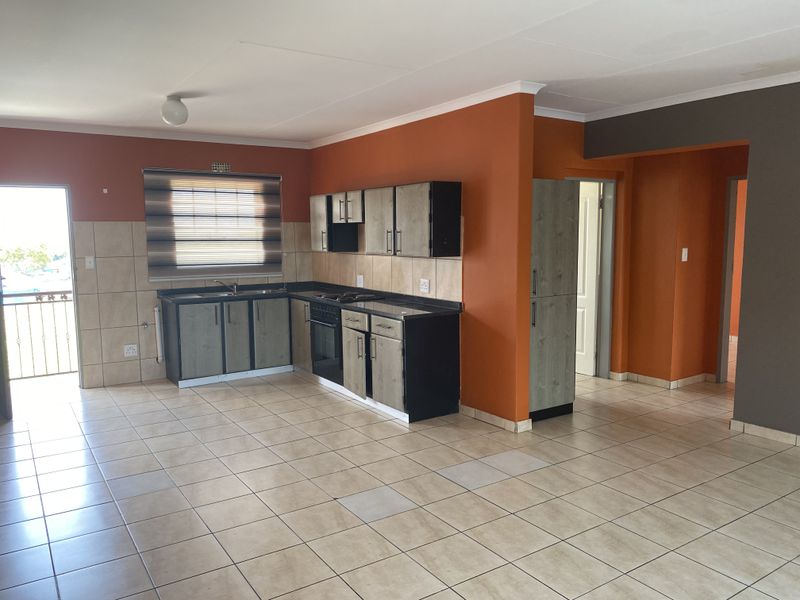 An open-plan kitchen featuring built-in cabinetry, a hob, oven, and tiled flooring, offering a functional layout ready for modern updates.