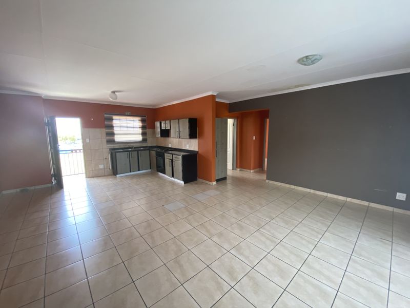 Spacious open-plan living and kitchen area featuring tiled flooring, built-in cabinetry, and direct access to an outdoor balcony.