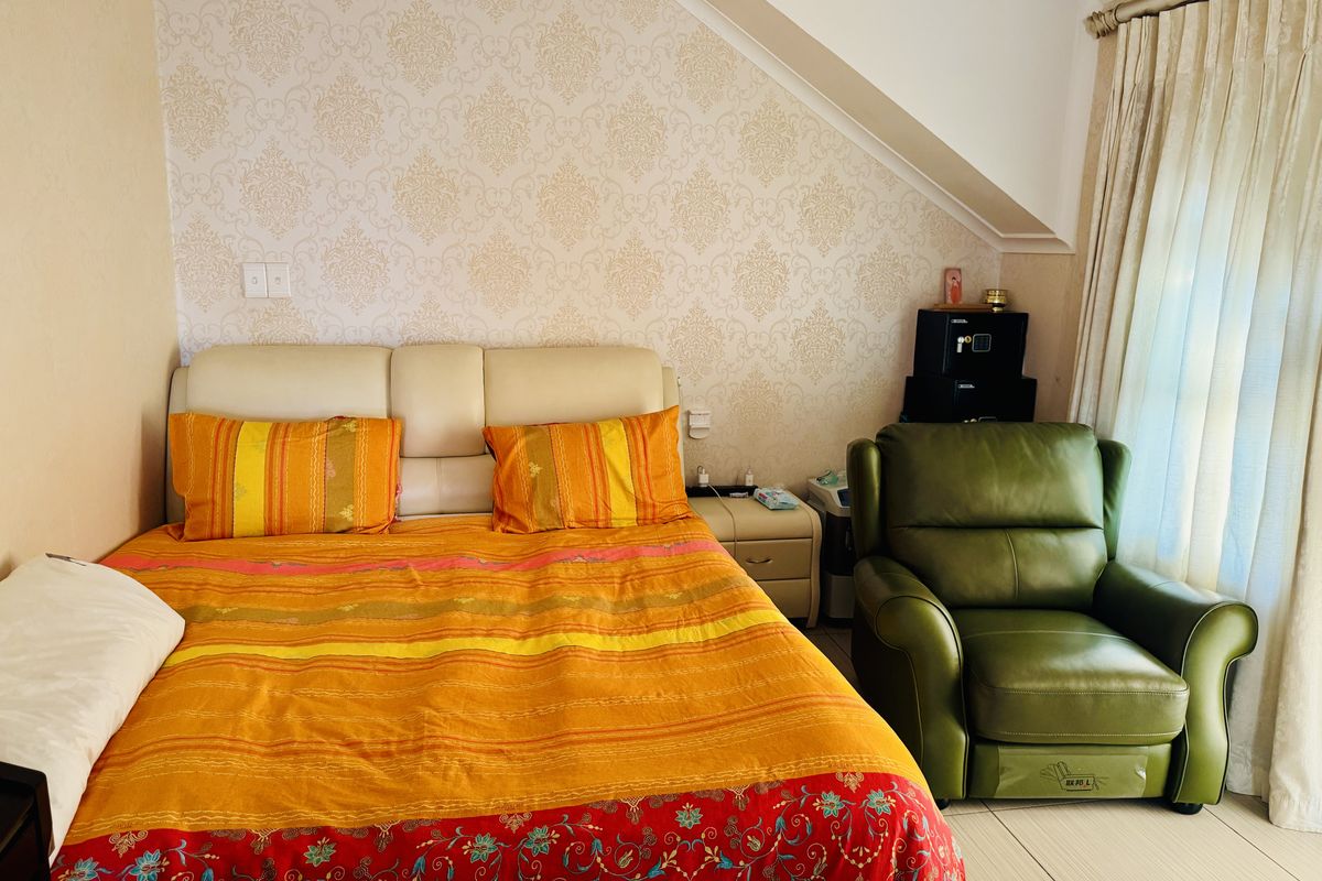 A bedroom featuring a sloped ceiling, patterned wallpaper, and large windows with curtains, providing a cozy and functional living space.