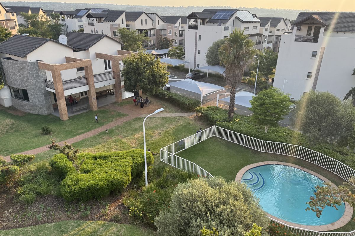 Elevated aerial view of the residential complex featuring landscaped gardens, a fenced swimming pool, paved walkways, and covered parking structures.