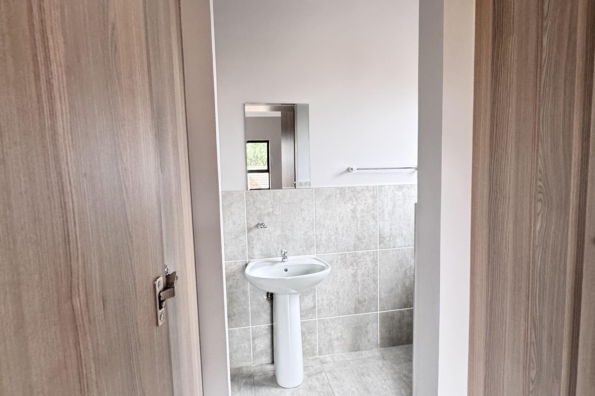 A clean, modern bathroom featuring a pedestal basin, tiled walls and flooring, and a wall-mounted mirror.