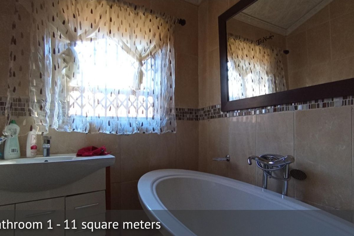 A bathroom featuring a freestanding bathtub, a vanity with a basin, and tiled walls with a decorative mosaic border.