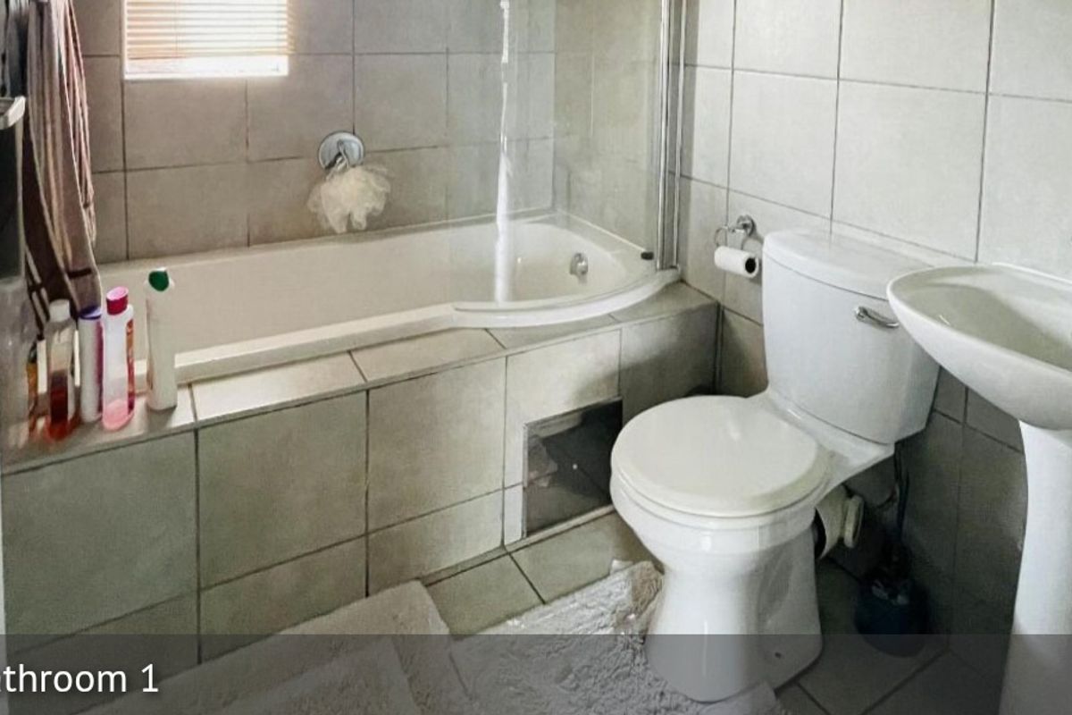 A functional bathroom featuring a tiled bathtub with a glass shower screen, a pedestal basin, and a standard toilet.