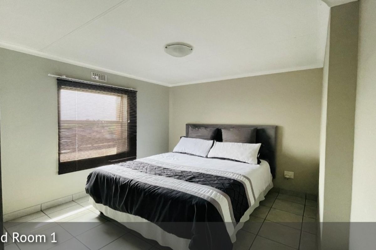 A well-lit bedroom featuring neutral wall tones, tiled flooring, and a window fitted with horizontal blinds.