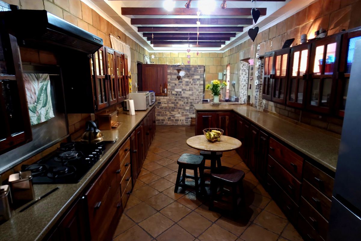 A rustic-style kitchen featuring exposed timber ceiling beams, brick walls, tiled flooring, and extensive built-in wooden cabinetry with stone countertops.