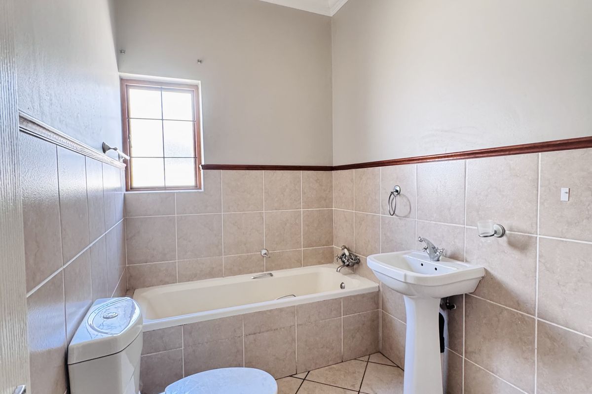 A functional bathroom featuring a built-in bathtub, pedestal basin, and toilet, finished with neutral wall and floor tiling.