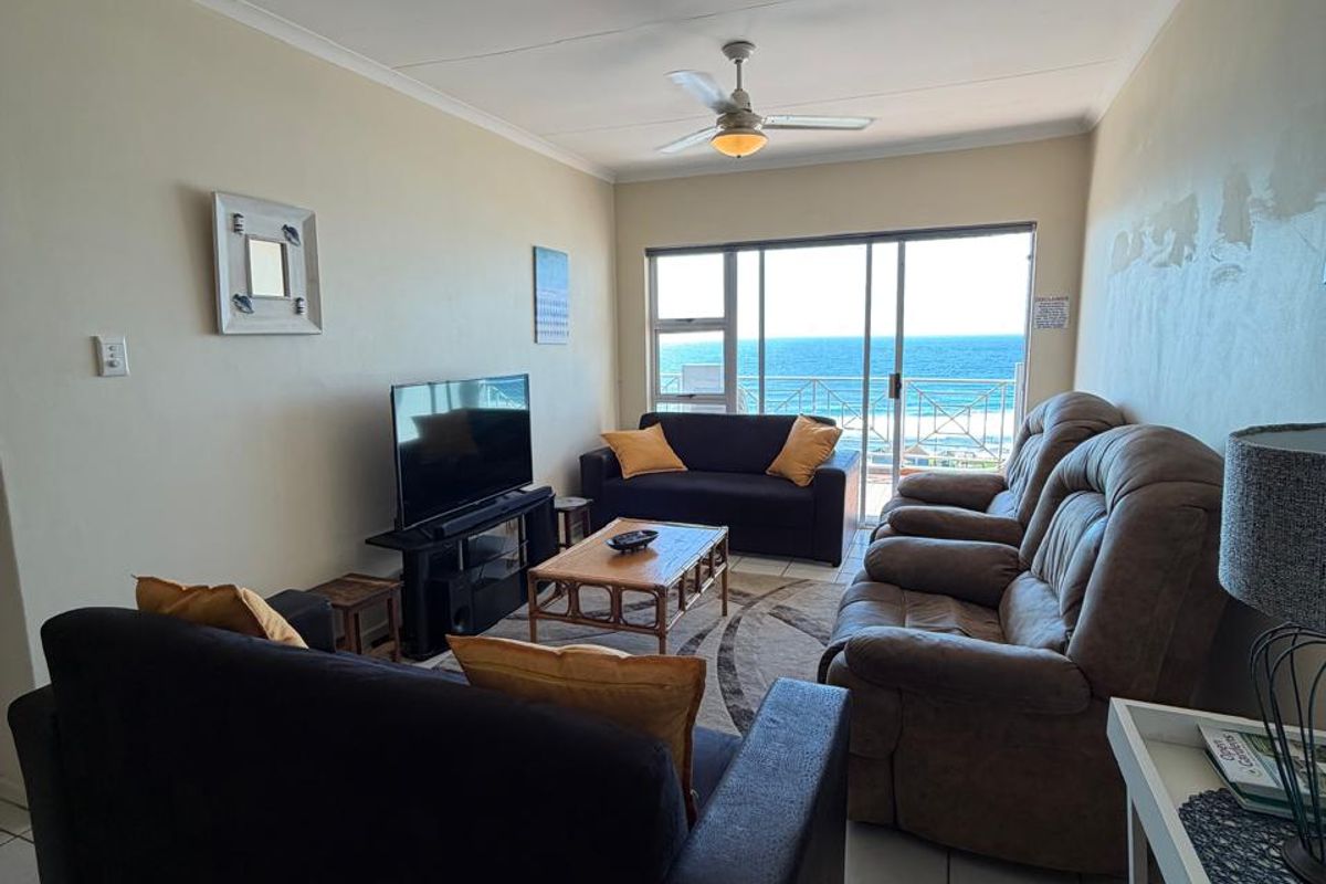 A living room featuring tiled flooring, a ceiling fan, and large sliding glass doors that open to a balcony with ocean views.