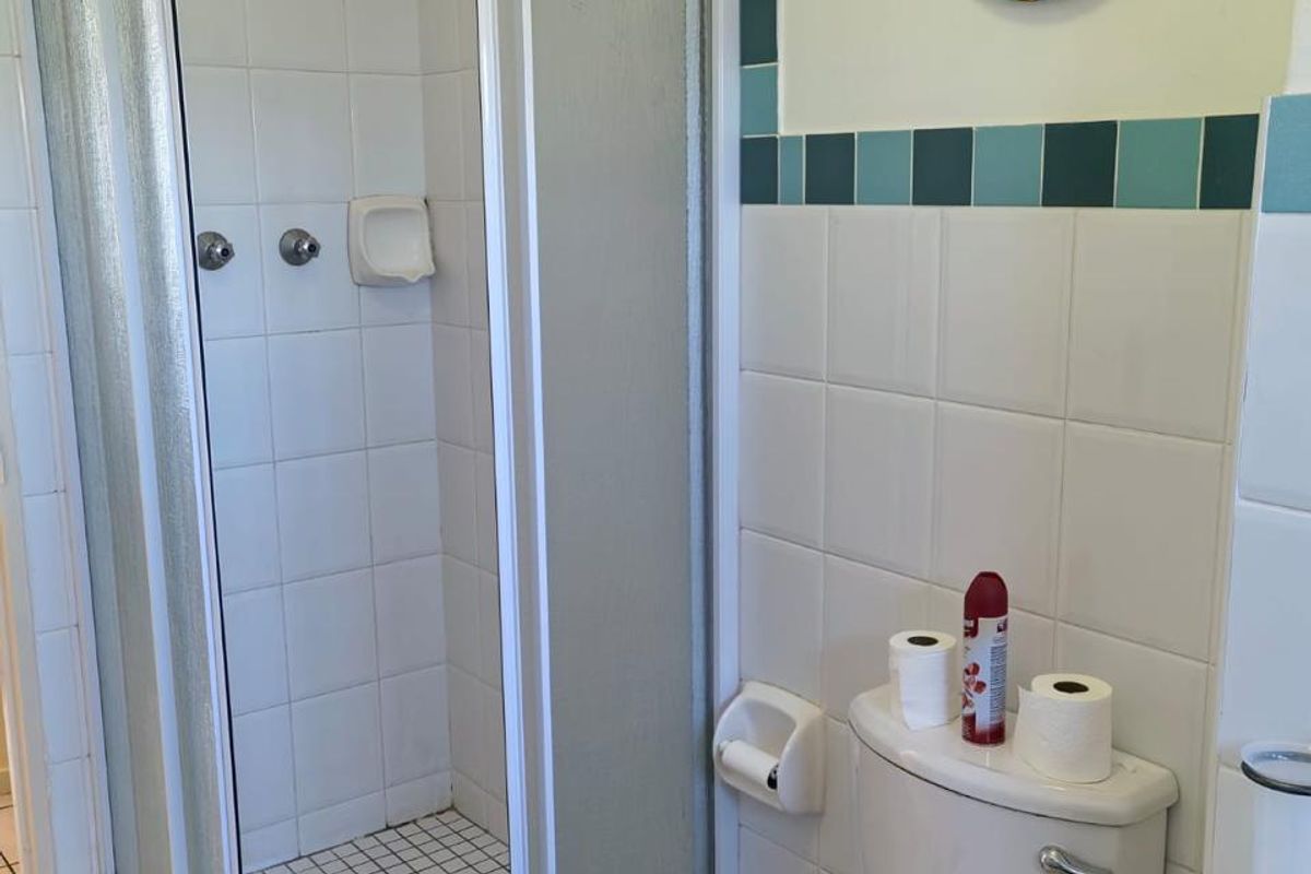 A functional bathroom featuring a corner shower enclosure, a standard toilet, and tiled wall accents.