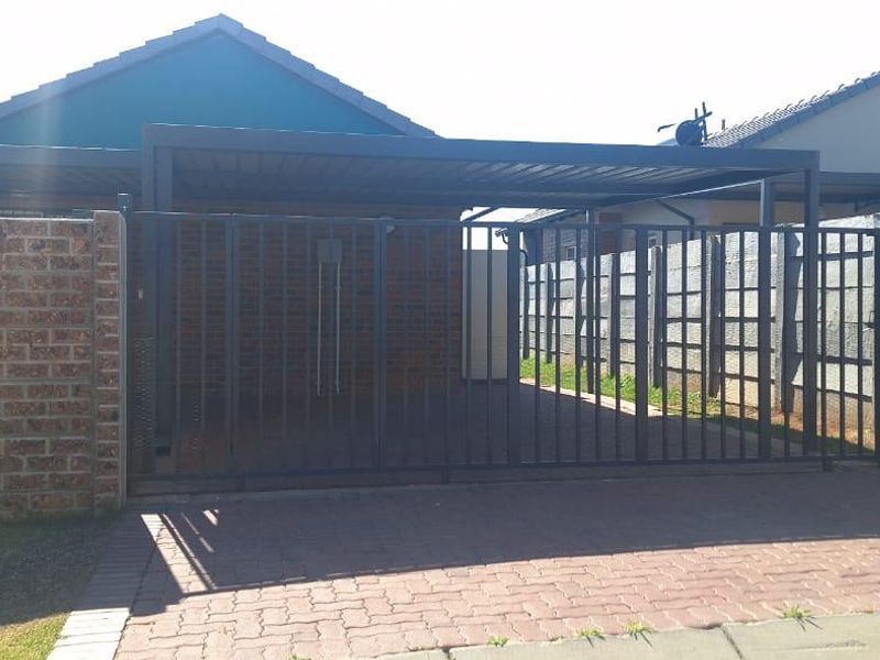 Front view of the property featuring a paved driveway, secure metal gate, and a covered carport structure.