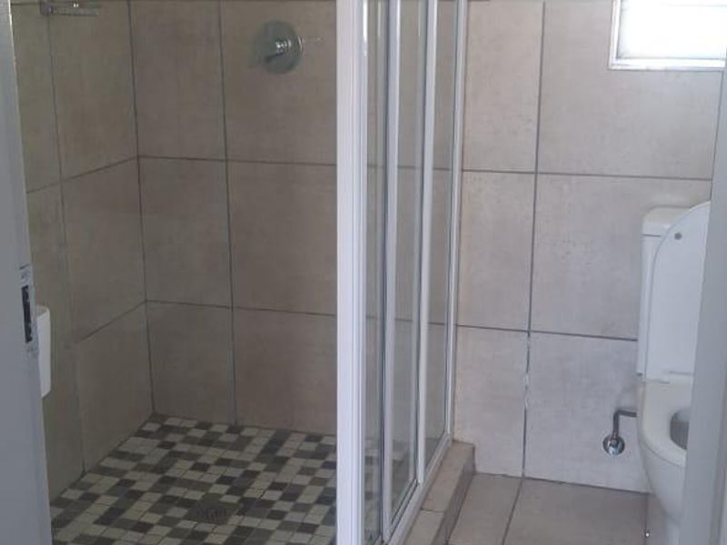 A functional bathroom featuring a corner shower enclosure with tiled walls and flooring, a standard toilet, and natural light from a side window.