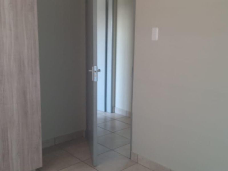 A simple, empty bedroom featuring neutral walls, tiled flooring, and a built-in wardrobe with a light wood finish.