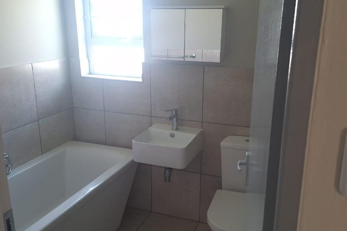 A compact, modern bathroom featuring a bathtub, wall-mounted basin, toilet, and neutral wall tiling.