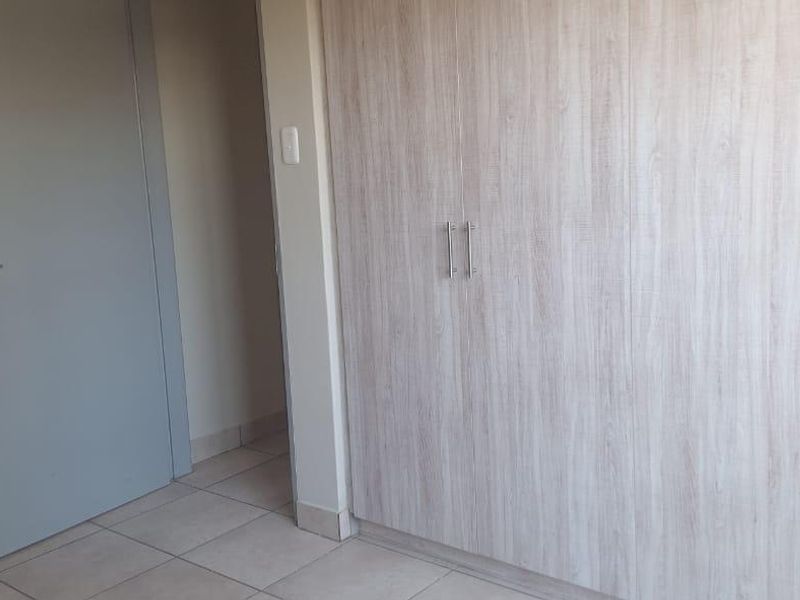 A clean, empty bedroom featuring light wood-finish built-in cupboards, tiled flooring, and direct access to an en-suite bathroom.