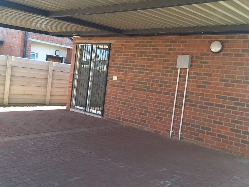 A covered carport area featuring brick wall construction, paved flooring, and a secure gated entrance to the property.