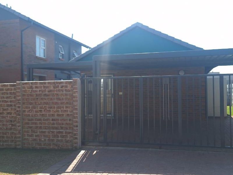 Front exterior view of the property featuring a brick boundary wall, metal security gate, and a covered carport over a paved driveway.