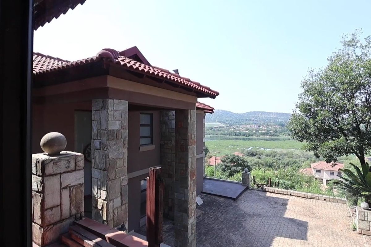 A view of the property's exterior rear facade featuring stone-clad pillars, a tiled roof, and a paved patio area overlooking a scenic landscape.
