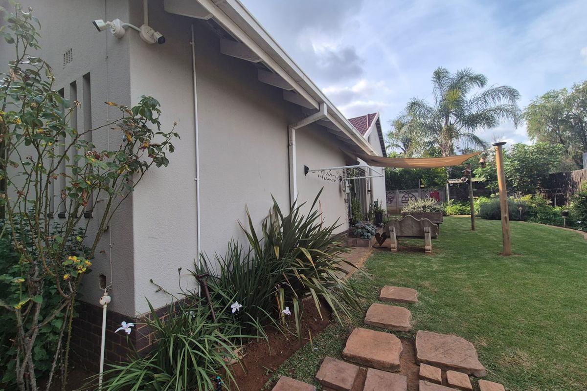 A view of the rear exterior of the house, featuring a well-maintained lawn, stone pathway, and a shaded outdoor area.