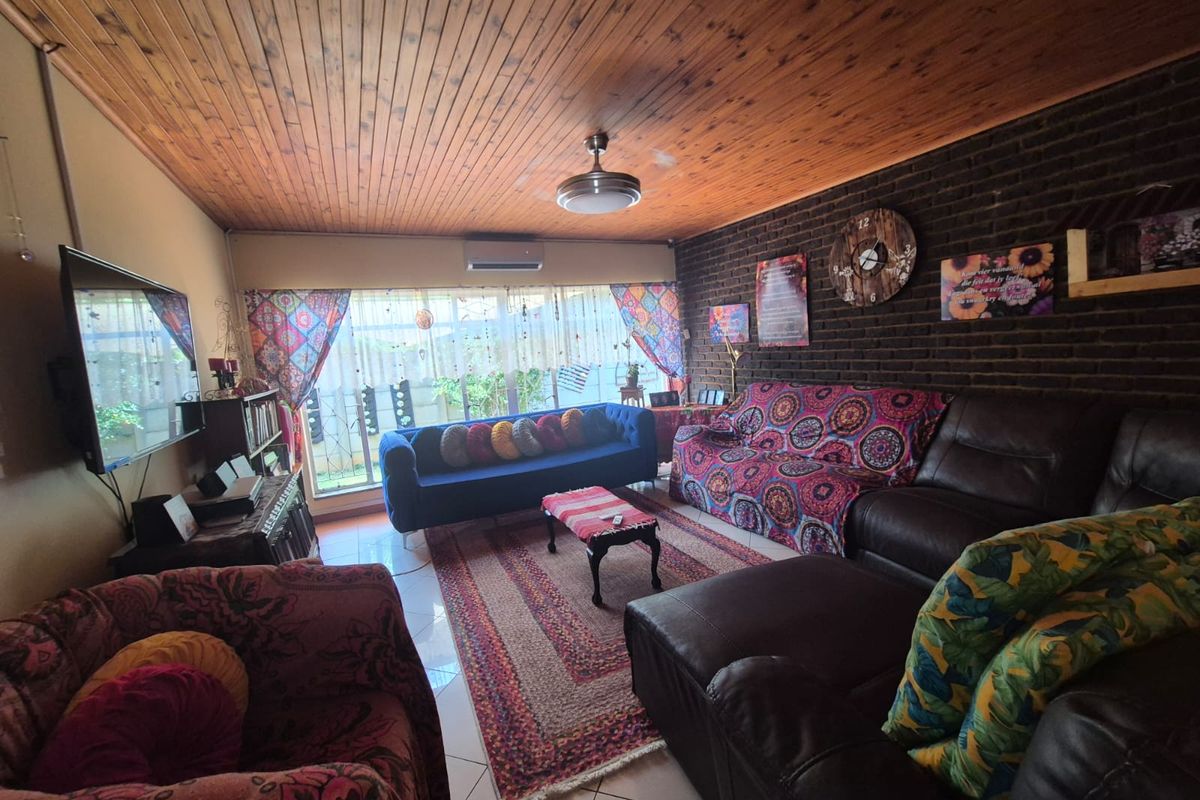 A living room featuring a dark brick feature wall, timber-clad ceiling, tiled flooring, and a wall-mounted air conditioning unit.