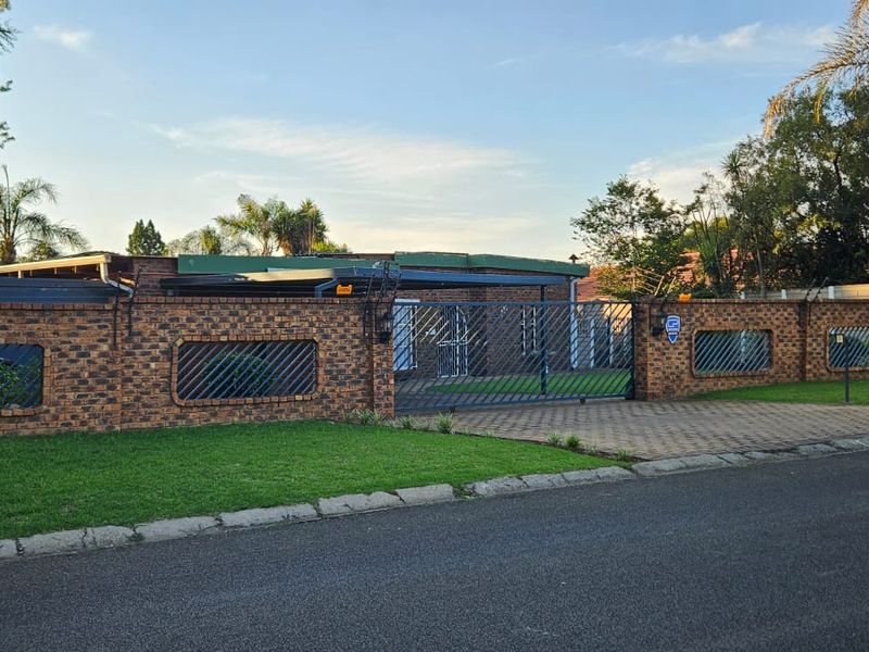 Front view of the property featuring a face brick boundary wall, paved driveway, and secure metal gate entrance.