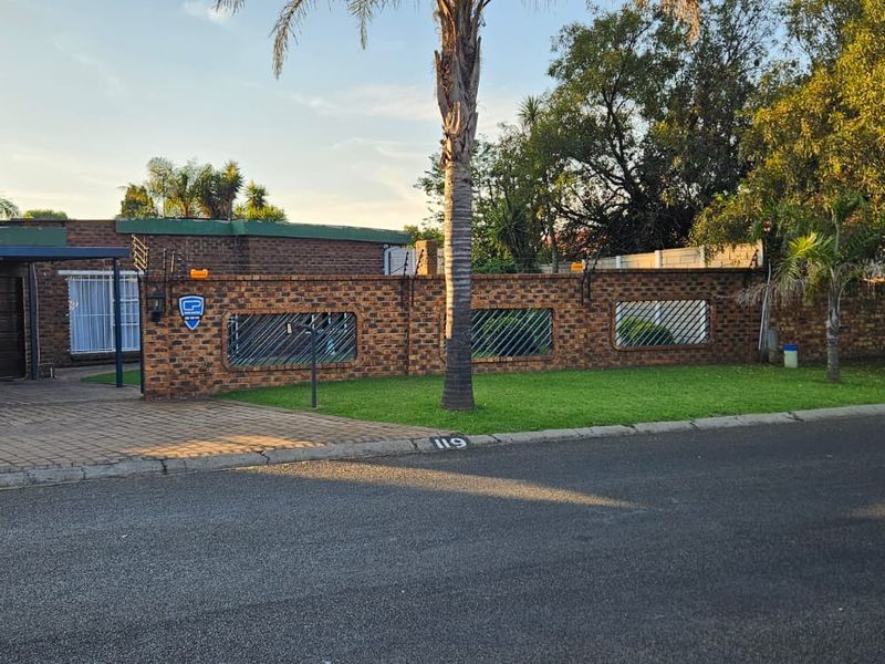 Front exterior view of the property featuring a brick boundary wall with security spikes, a paved driveway, and a covered carport.