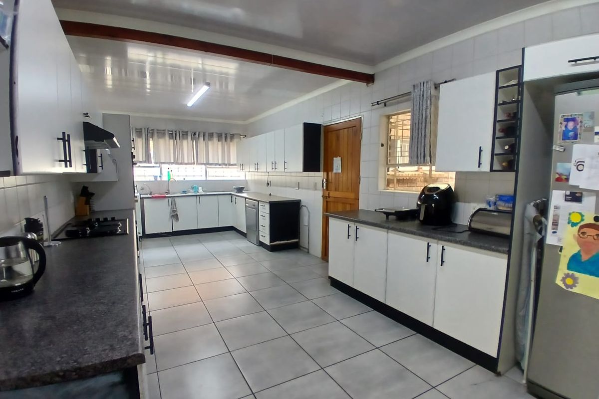 Spacious kitchen featuring white cabinetry, dark laminate countertops, tiled flooring, and a functional layout with integrated hob and extractor fan.