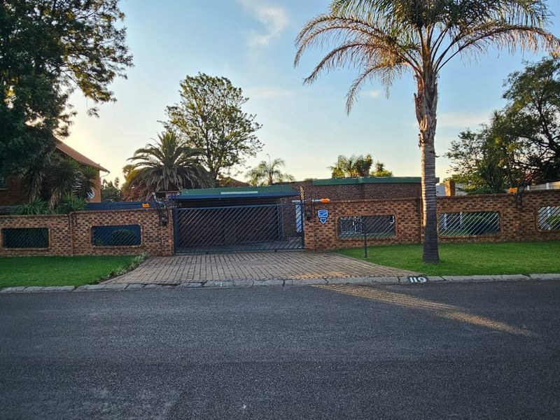 Front view of the property featuring a brick boundary wall, paved driveway, and secure metal gate entrance.