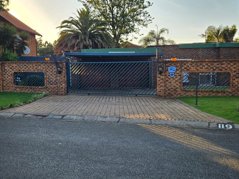 Front view of the property featuring a brick boundary wall, paved driveway, and a secure sliding metal gate with an integrated carport.