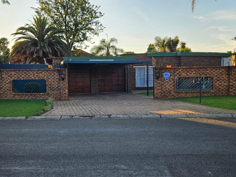 Front exterior view of a brick house featuring a paved driveway, double garage, and secure boundary wall with electric fencing.