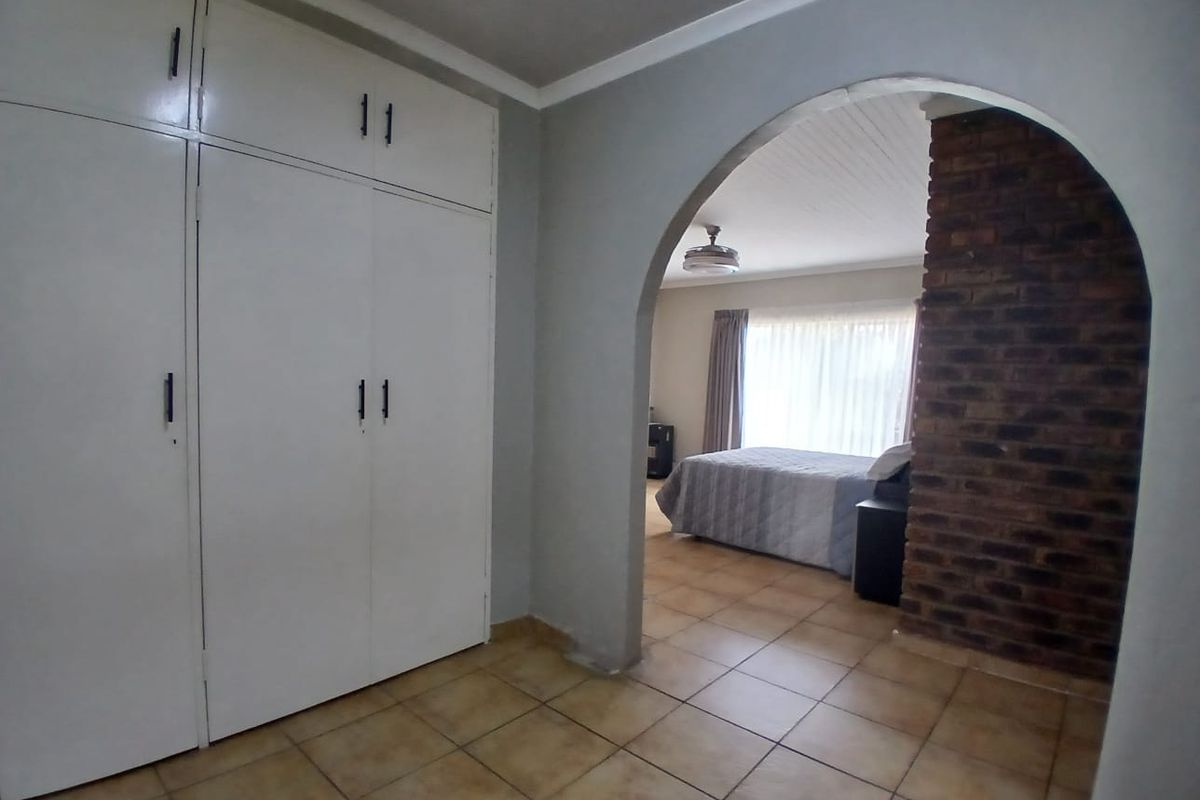 Bedroom featuring built-in cupboards, tiled flooring, and a distinctive brick feature wall with an arched transition to the sleeping area.