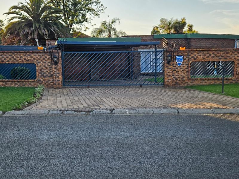 Front view of the property featuring a brick boundary wall, paved driveway, and a secure sliding gate with an integrated carport.